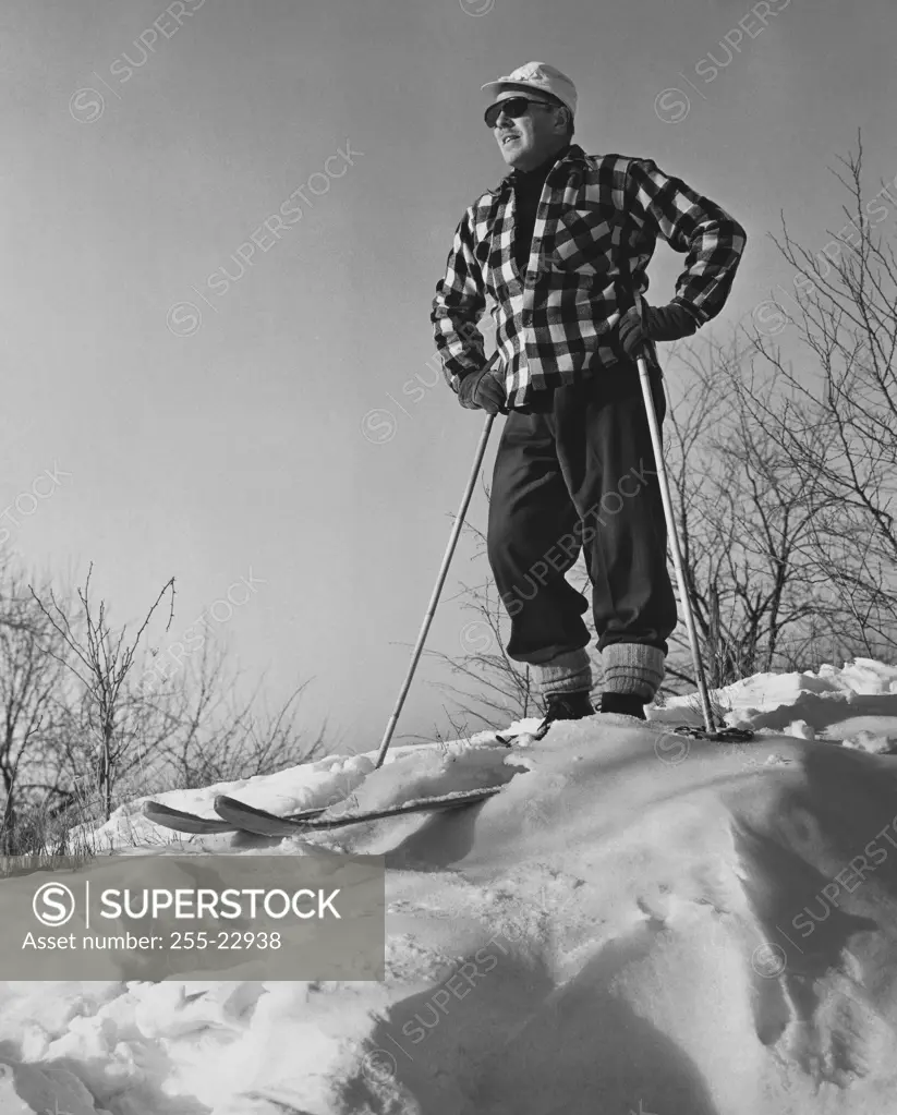 Low angle view of a mature man holding ski poles and standing on snow