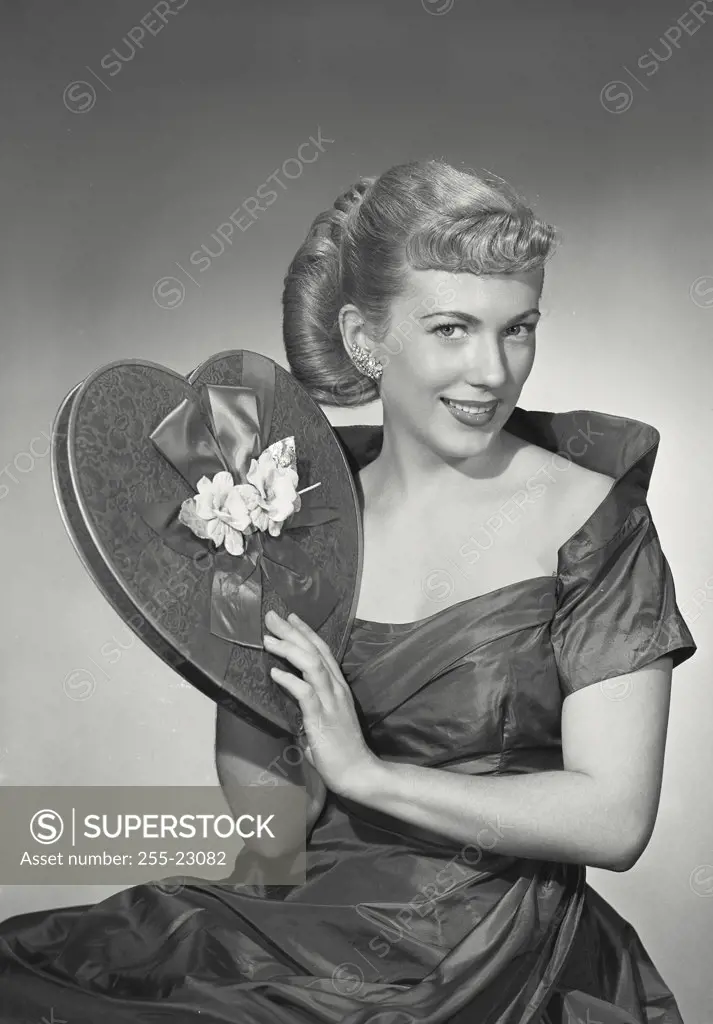 Vintage photograph. Woman in elegant dress smiling and holding heart-shaped box of chocolates