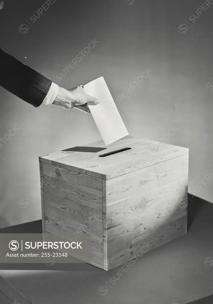 Vintage photograph. Close-up of a man's hand placing folded ballot into slot in wooden box
