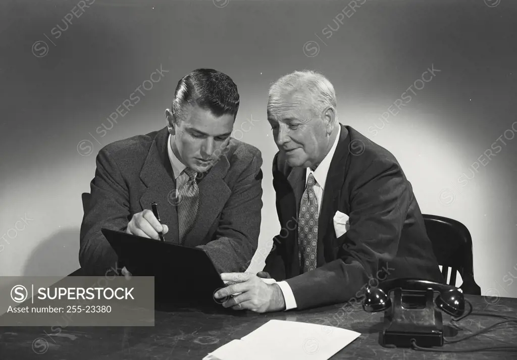 Young man and older man sitting together at desk discussing papers