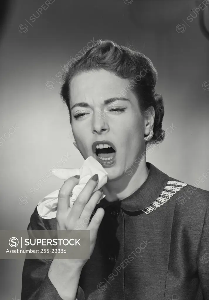 Vintage Photograph. Woman wearing buttoned up blouse sneezing into tissue