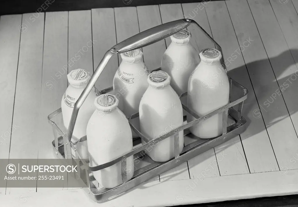 Six pack of milk bottles sitting on wooden surface