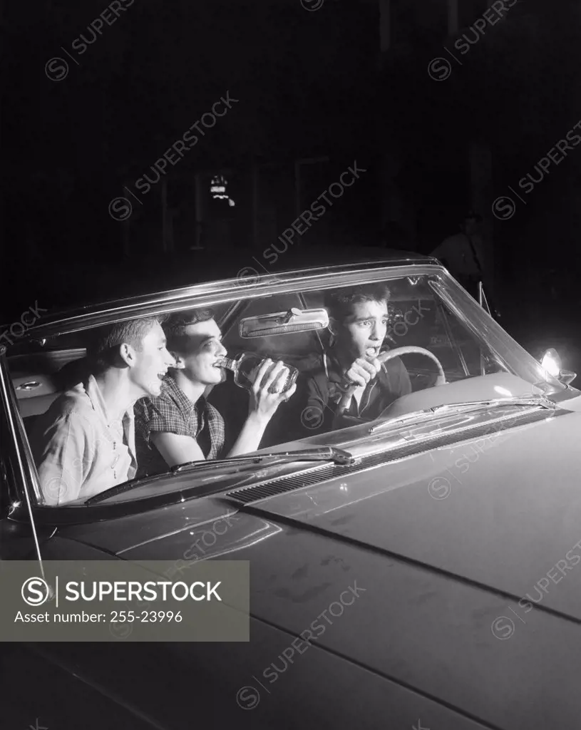 High angle view of a teenage boy driving a car while his friends drink beside him