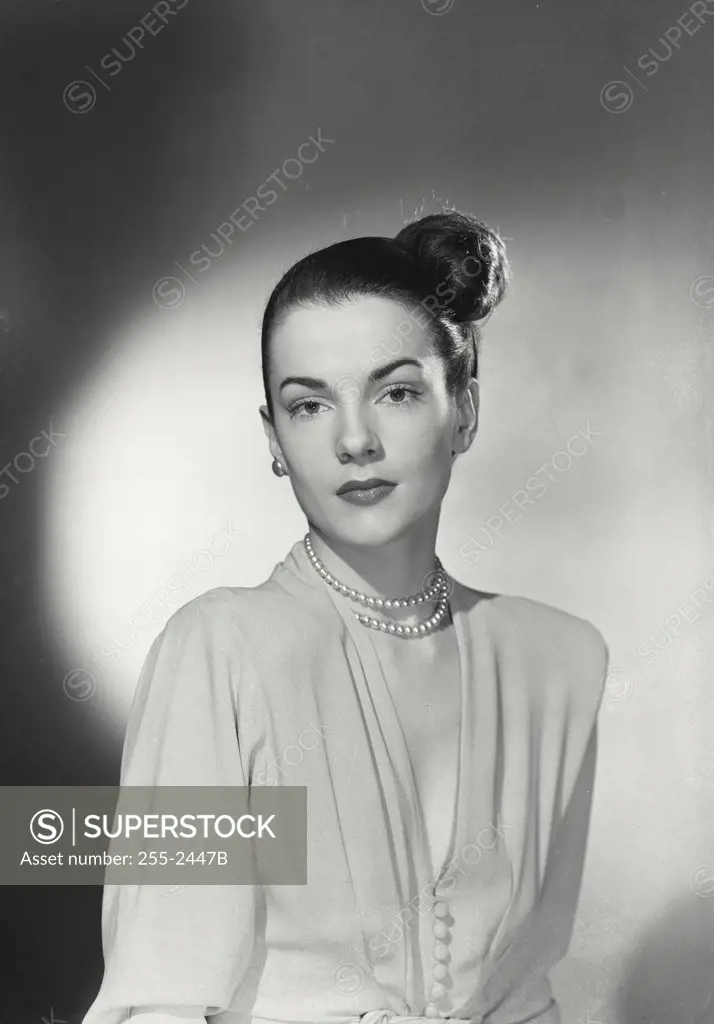Glamorous woman with dark hair in side bun wearing pearl necklace and nice blouse with serious expression