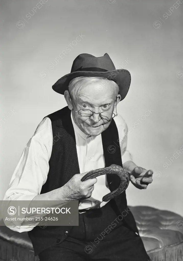 Vintage Photograph. Old man with glasses wearing hat and wool vest about to throw horseshoe