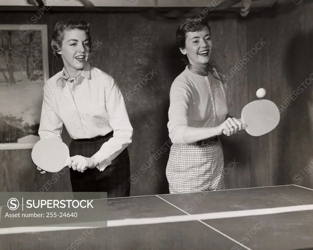 Two young adult women playing ping pong