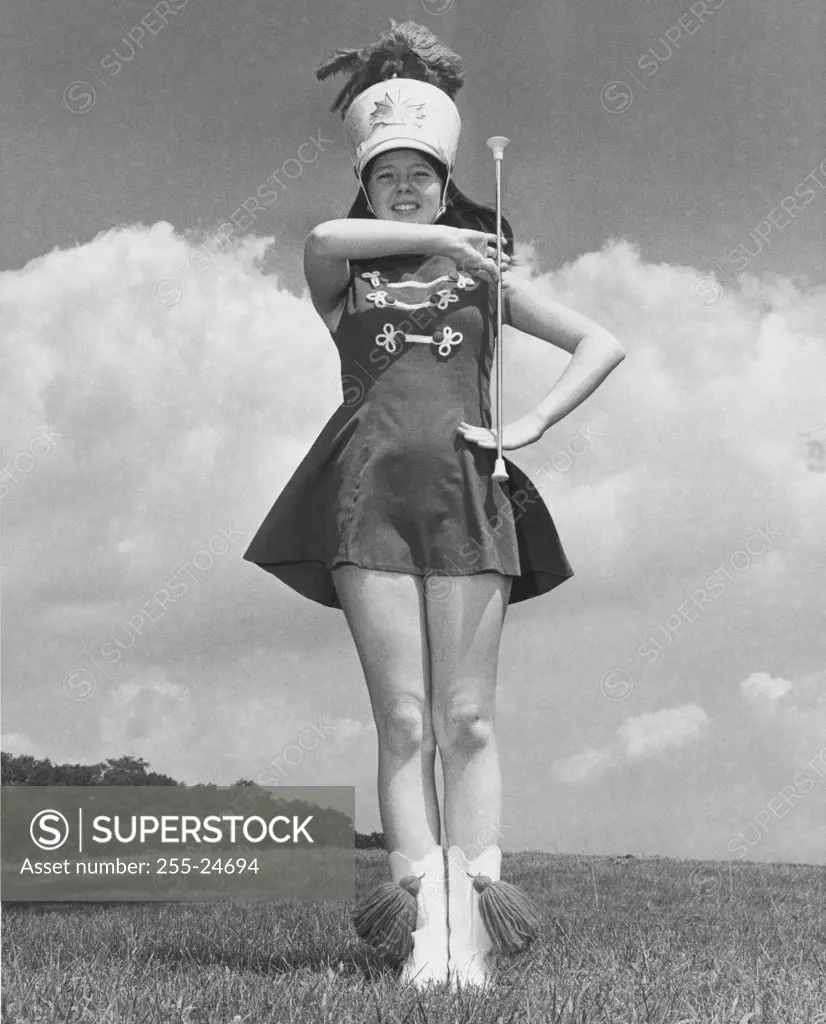 Low angle view of a drum majorette performing with a twirling baton in a field and smiling