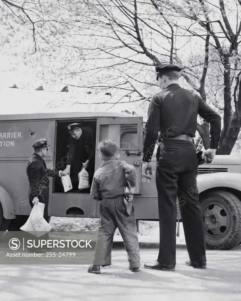 Rear view of a boy imitating a security guard and standing near an armored truck