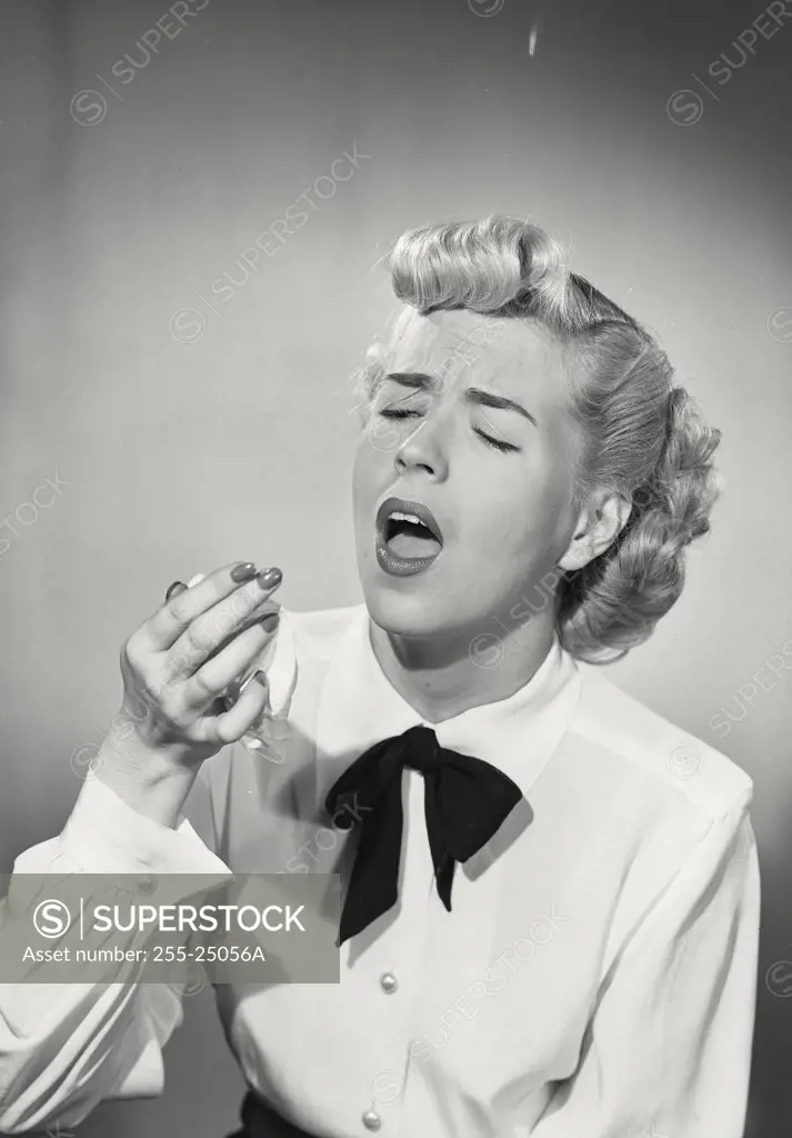 Vintage photograph. Woman in button shirt and western bowtie sneezing into handkerchief