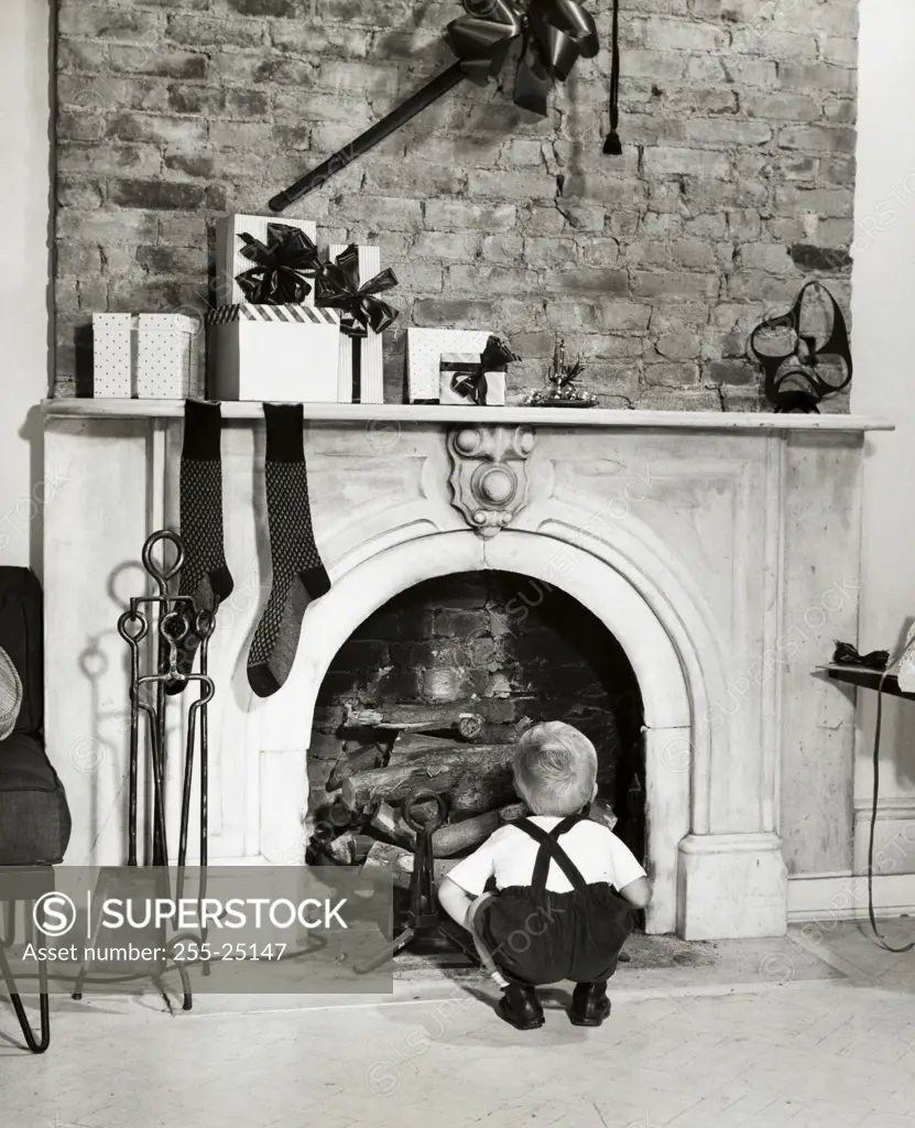 Rear view of a boy crouching near a fireplace