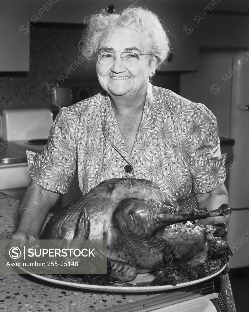 Close-up of senior woman holding platter of roast turkey in kitchen, smiling