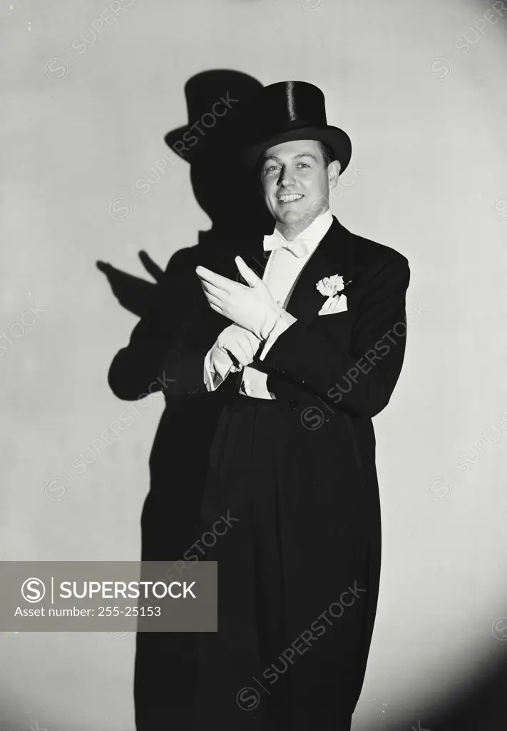 Vintage Photograph. Man wearing tuxedo and top hat adjusting gloves