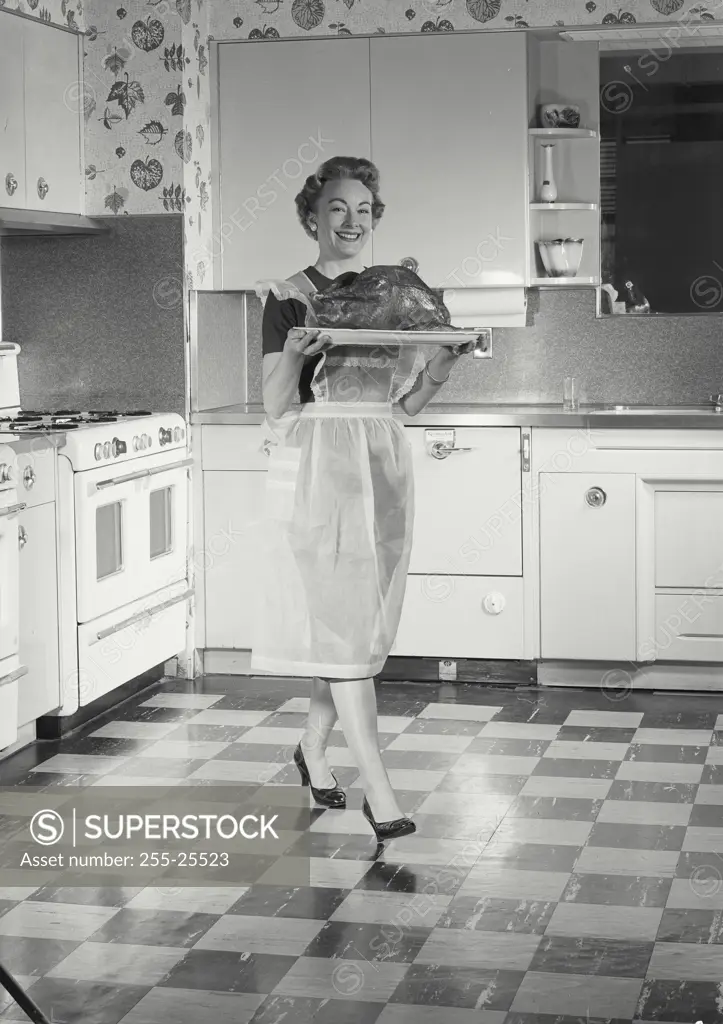 Vintage Photograph. Woman in kitchen carrying turkey.