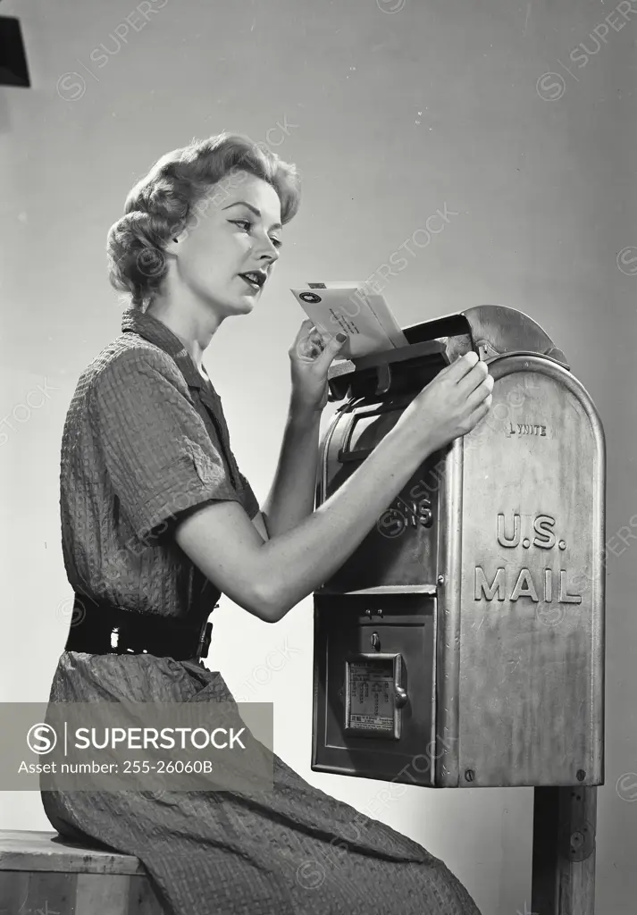 Vintage Photograph. Woman sitting placing envelopes into top slot of US Mail Box
