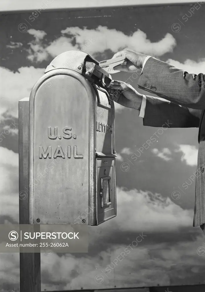 Vintage Photograph. Male hands placing envelopes into top slot of US Mail letter box in front of cloud sky background