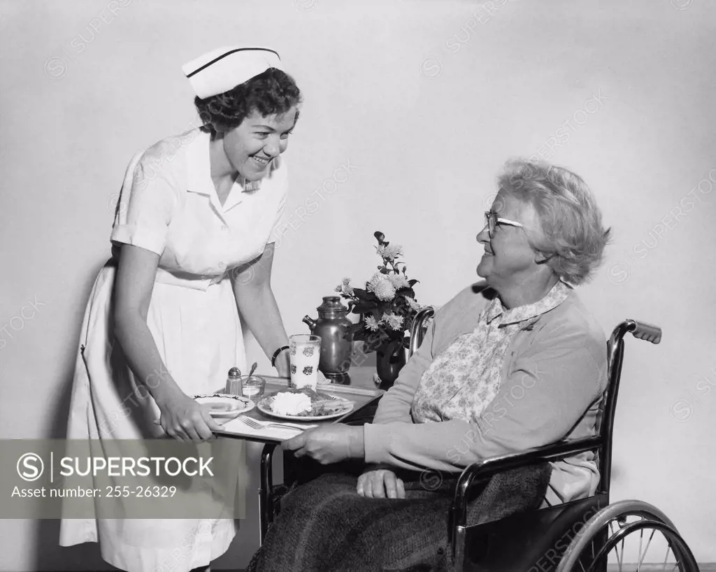 Side profile of a female nurse serving food to a senior woman sitting in a wheelchair