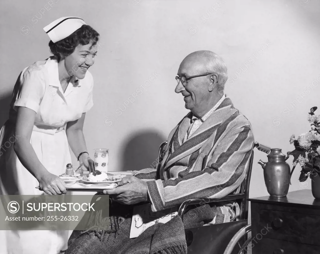 Side profile of a female nurse serving food to a senior man sitting in a wheelchair