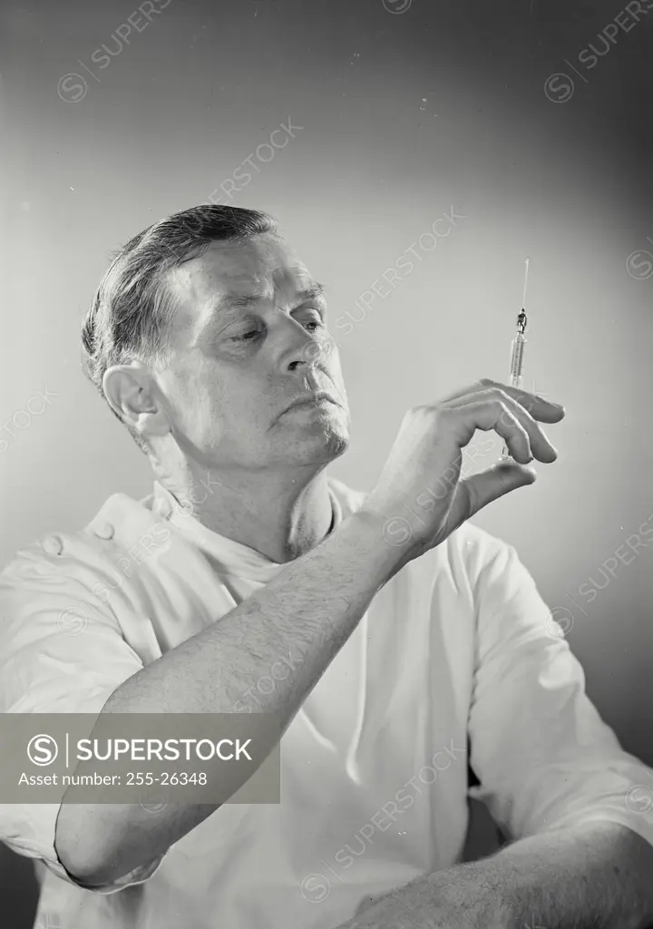 Vintage Photograph. Man wearing doctor's smock inspecting a syringe in his hand