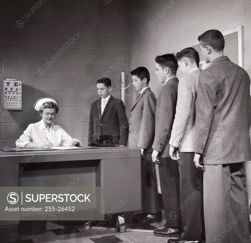 Teenage boys standing in a row beside a nurse's desk