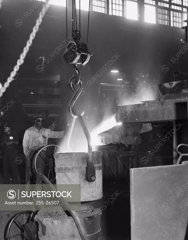 Vintage Photograph. Male worker overseeing molten iron being poured into a bucket at an iron foundry