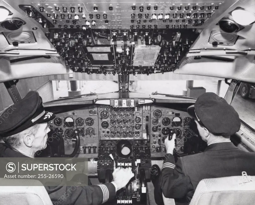 Rear view of two pilots sitting in the cockpit of an airplane