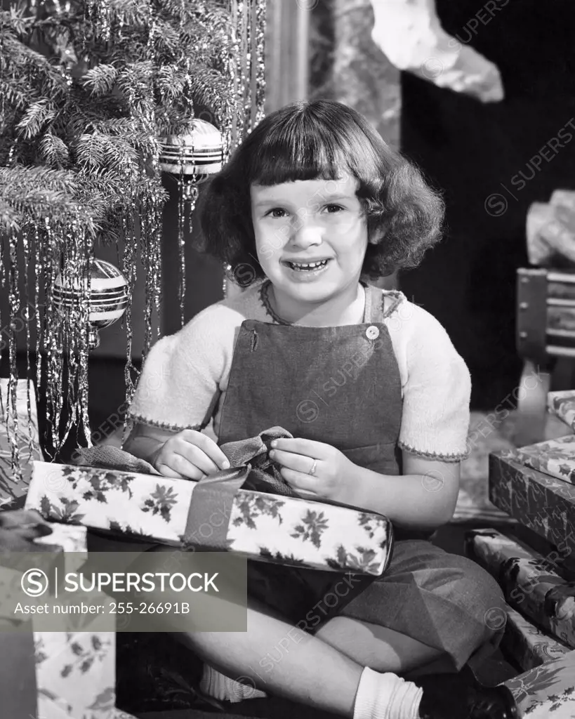 Vintage Photograph. Young girl opening Christmas gift next to the tree