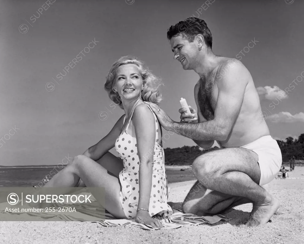 Young man applying suntan lotion on a young woman's back at the beach
