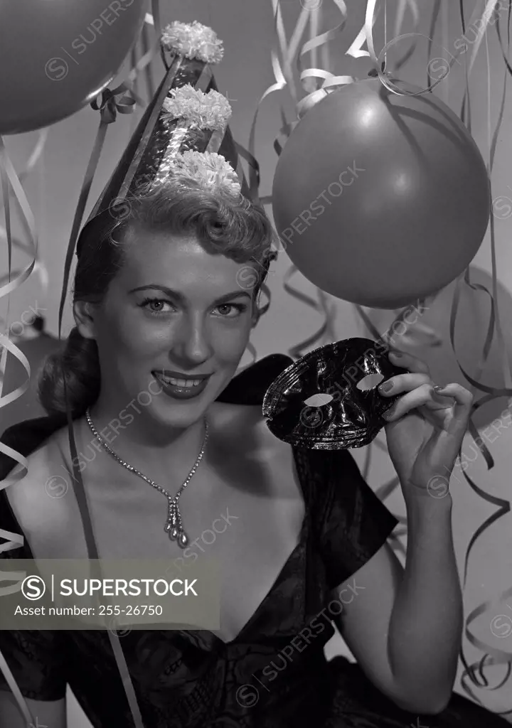 Studio portrait of woman wearing party hat and holding carnival mask