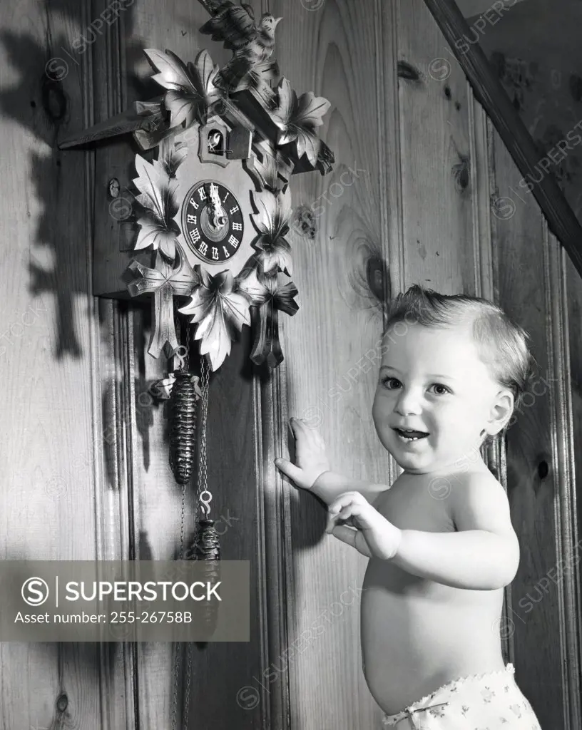 Side profile of a baby boy standing near a cuckoo clock and smiling