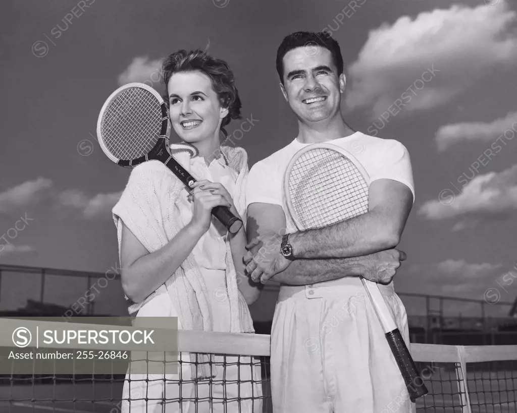 Close-up view of young couple holding tennis rackets and smiling