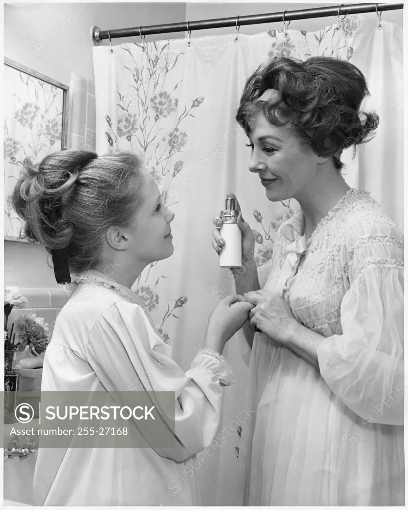 Mother about to spray perfume on her daughter