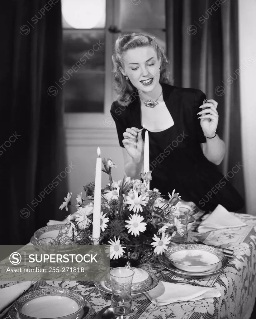 Young woman lighting candle at dining table