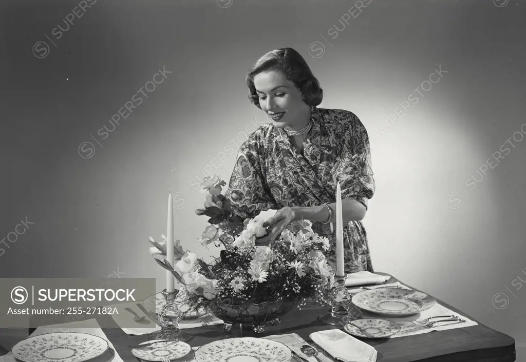 Woman lighting candles in centerpiece at dinner table.