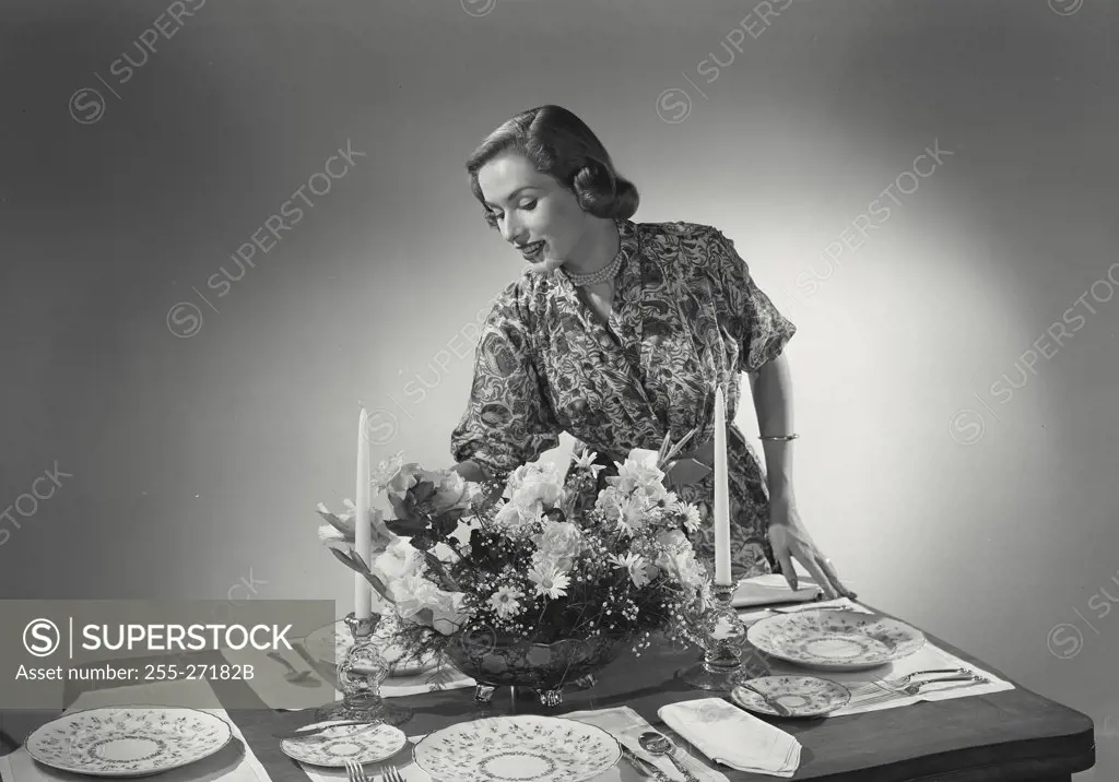 Woman adjusting centerpiece at dinner table.
