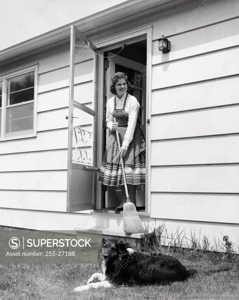 Young woman standing at the doorstep holding a broom stick