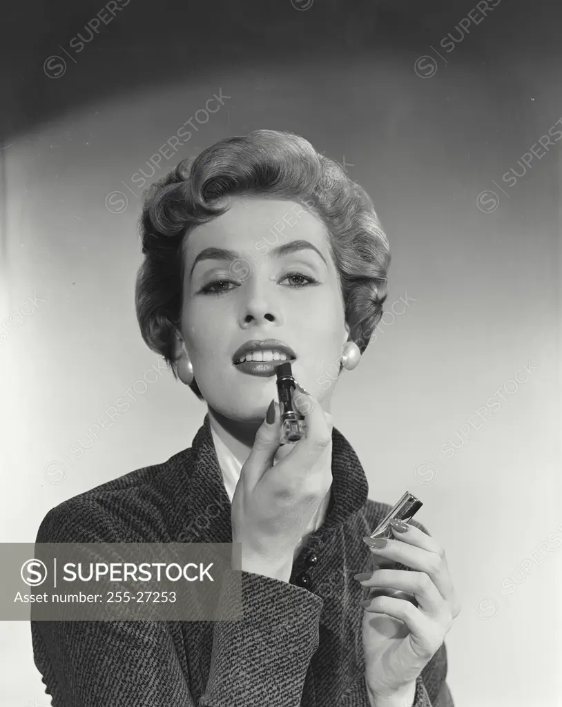 Vintage Photograph. Woman with short hairstyle putting on lipstick looking at camera