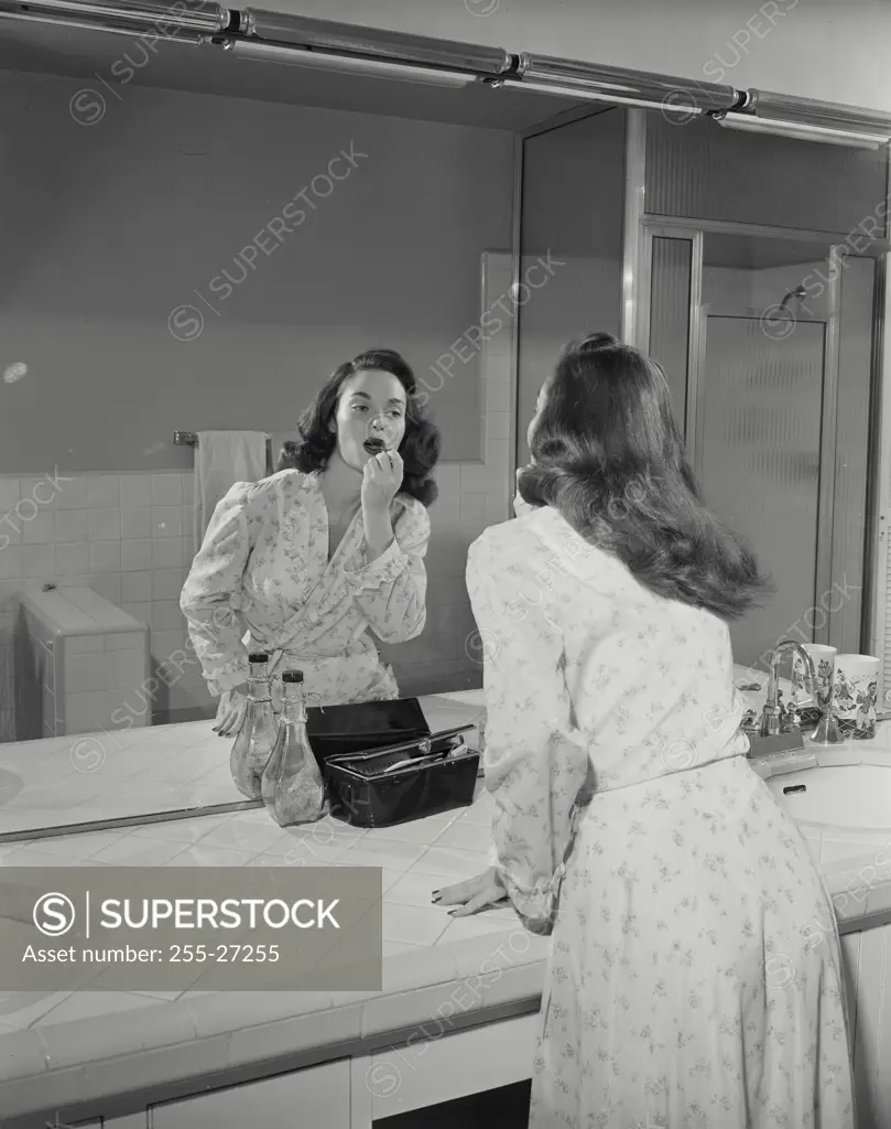 Vintage Photograph. Woman wearing bathrobe getting ready in bathroom mirror putting on lipstick
