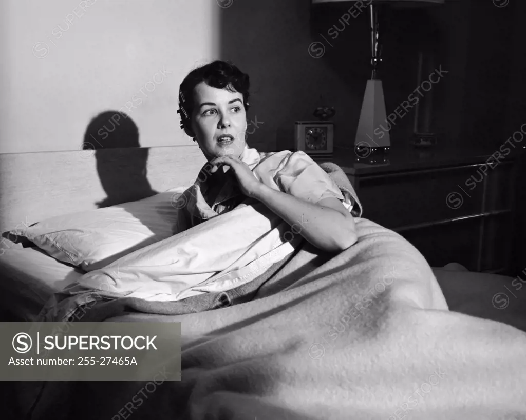 Young woman lying on the bed and looking afraid