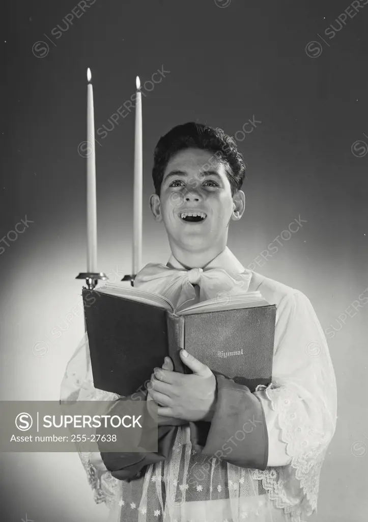 Altar boy singing while holding hymnal book with candles in background
