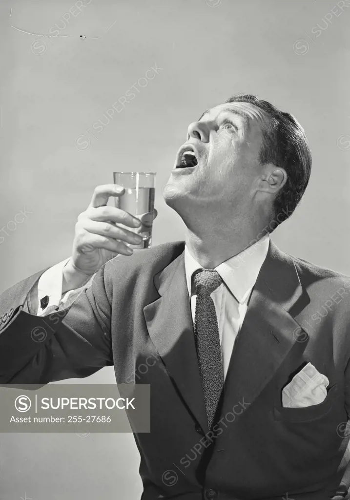 Vintage Photograph. Man in suit holding glass with shocked expression looking up
