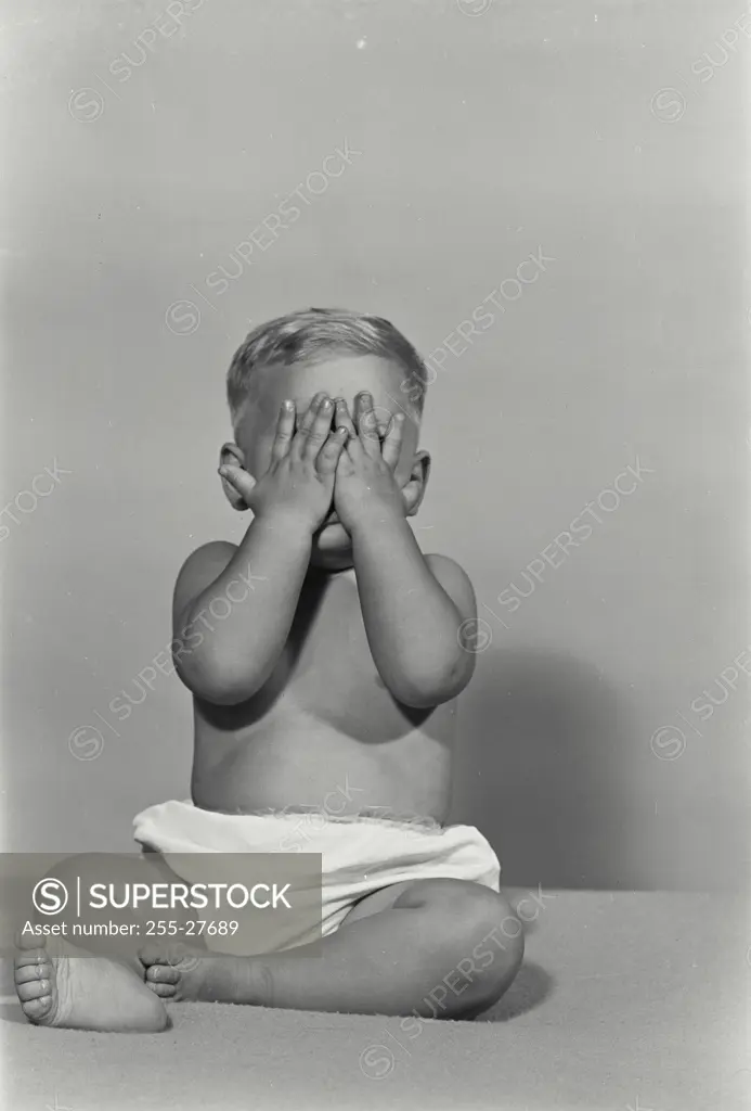 Vintage Photograph. Baby sitting on blanket covering up face with hands
