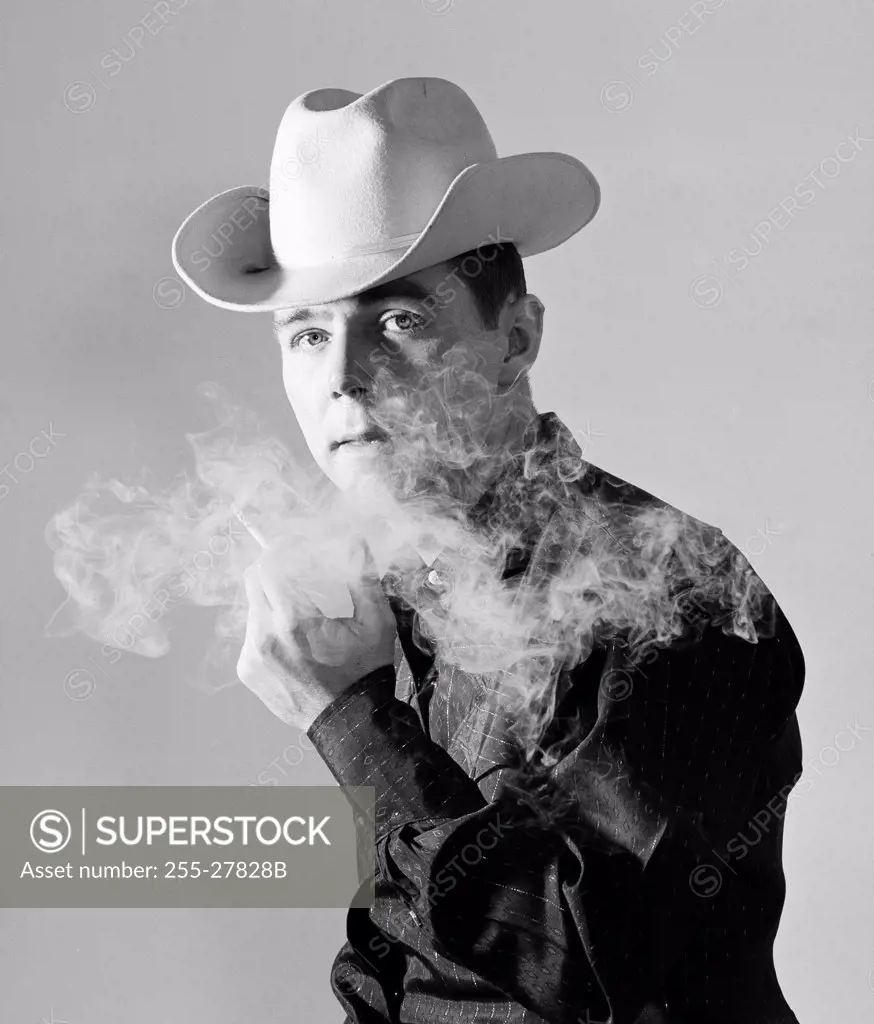 Studio portrait of man wearing cowboy hat smoking cigarette