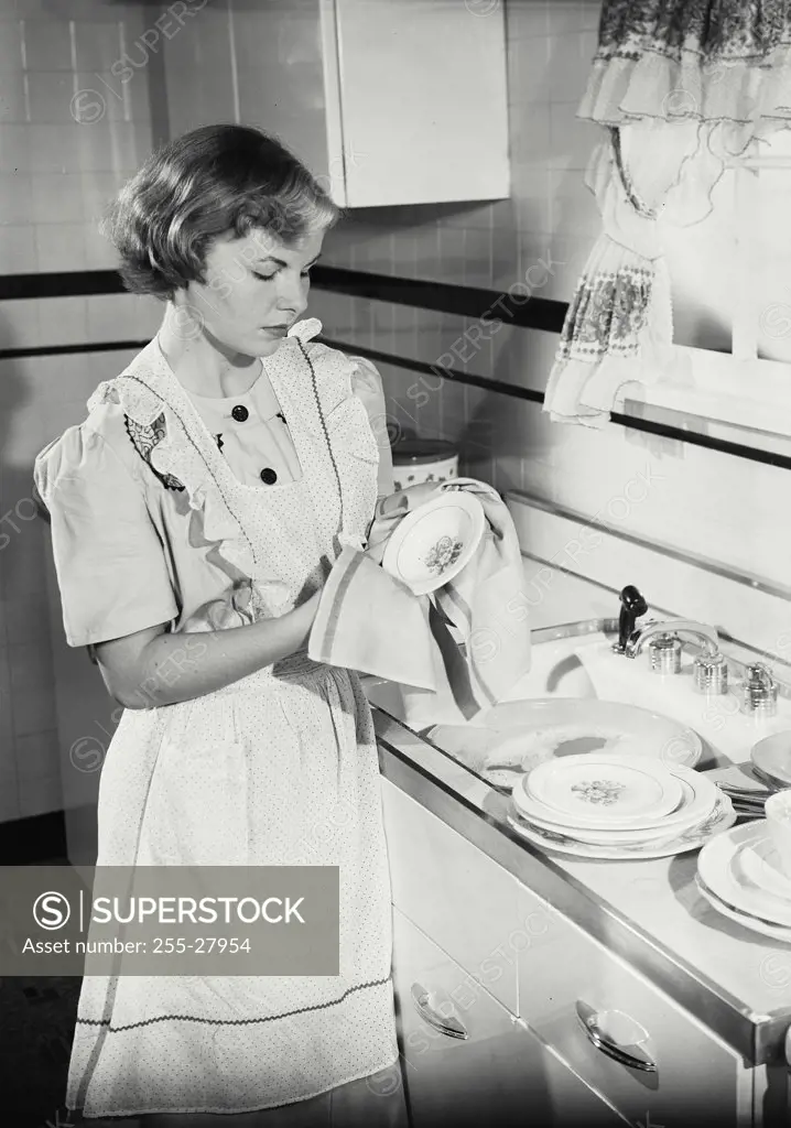 Vintage photograph. Young woman cleaning dishes in kitchen