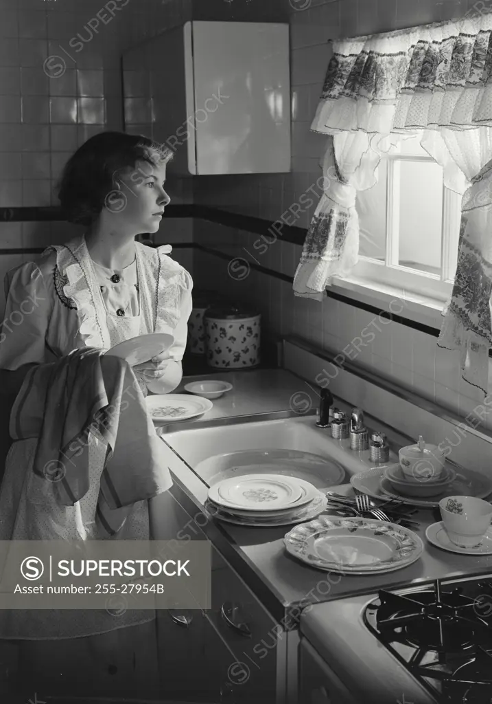 Vintage photograph. Young woman washing dishes and looking out window