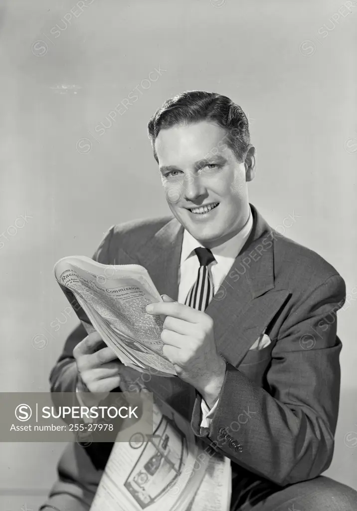 Vintage Photograph. Smiling brunette man in suit holding up newspaper