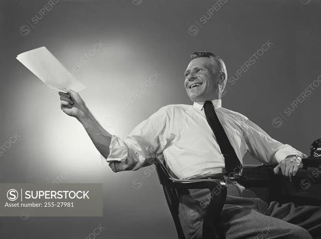 Vintage Photograph. Man in button shirt and tie leaning back and passing a document. Frame 2