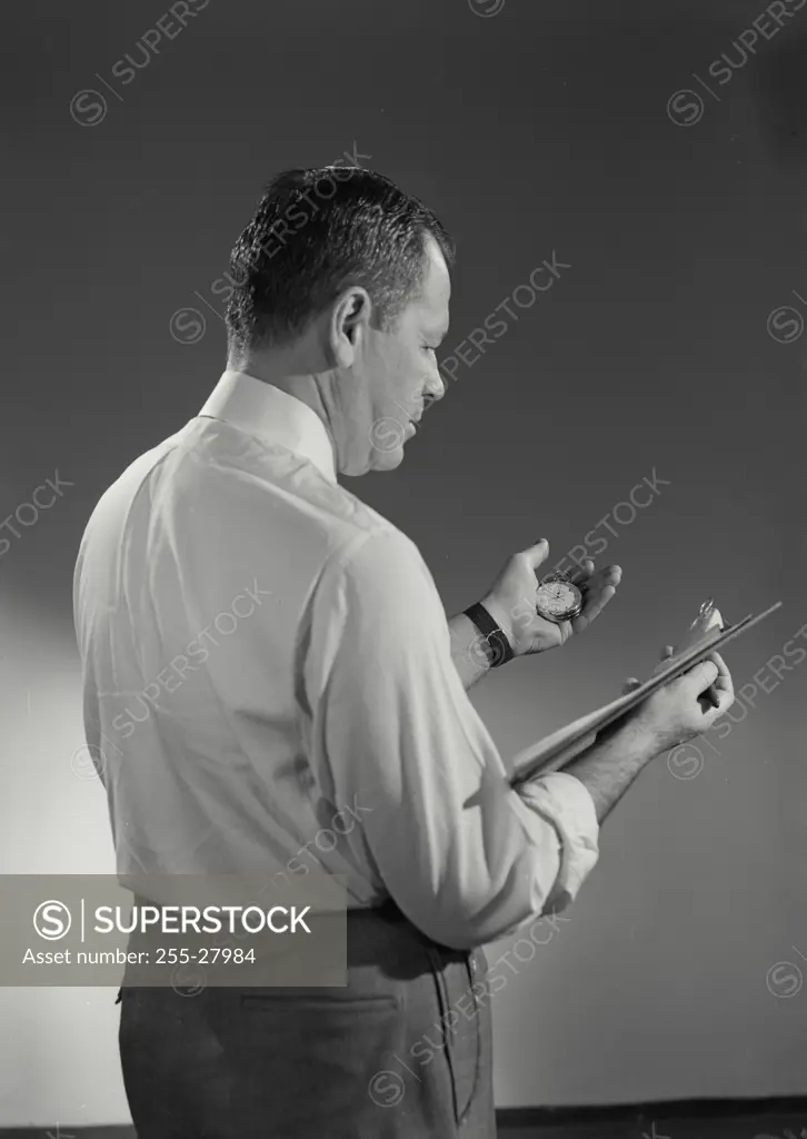 Vintage Photograph. Man wearing dress shirt holding stopwatch and clipboard