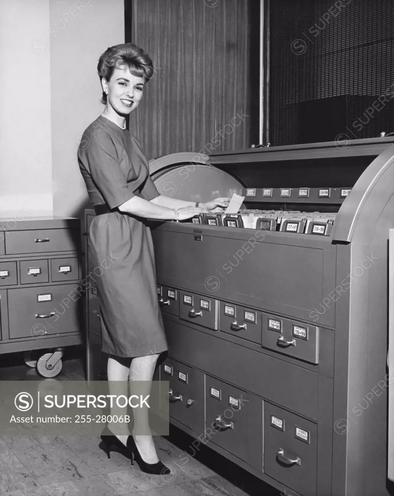 Portrait of a businesswoman holding a document beside a filing cabinets