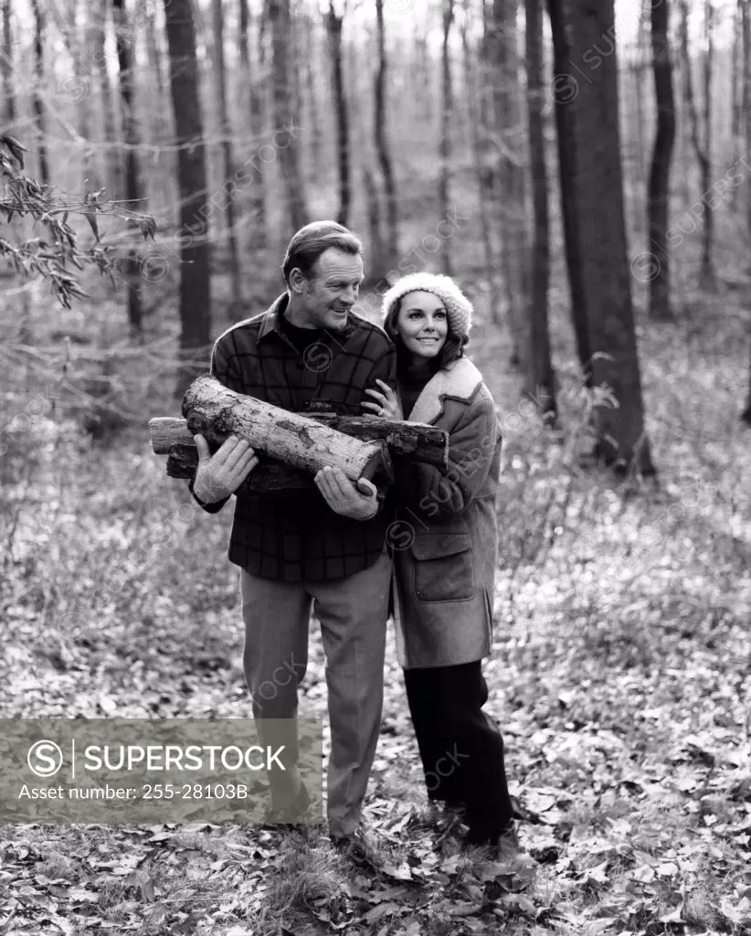 Mature couple in forest, man holding firewood