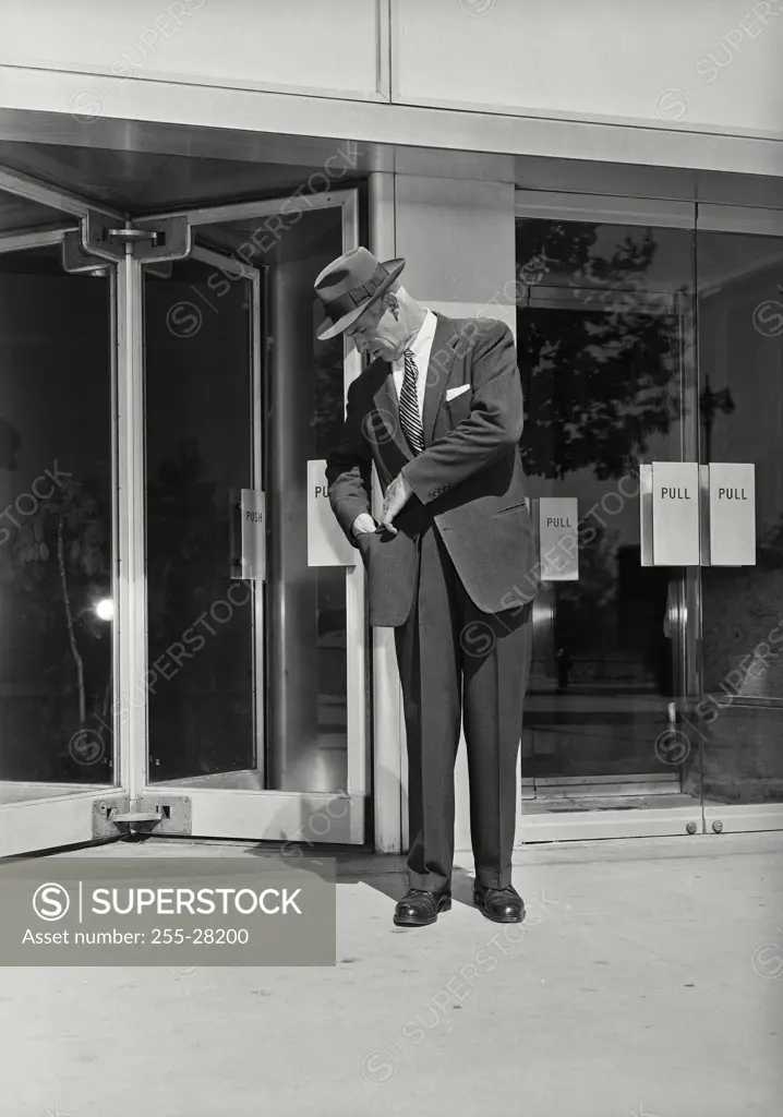 Vintage Photograph. Businessman in suit standing in front of building with revolving door checking his jacket pocket